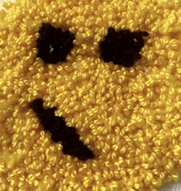 a yellow crocheted emoji face with black eyes